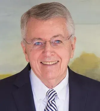 Smiling man in a dark suit and striped tie against a soft painted background