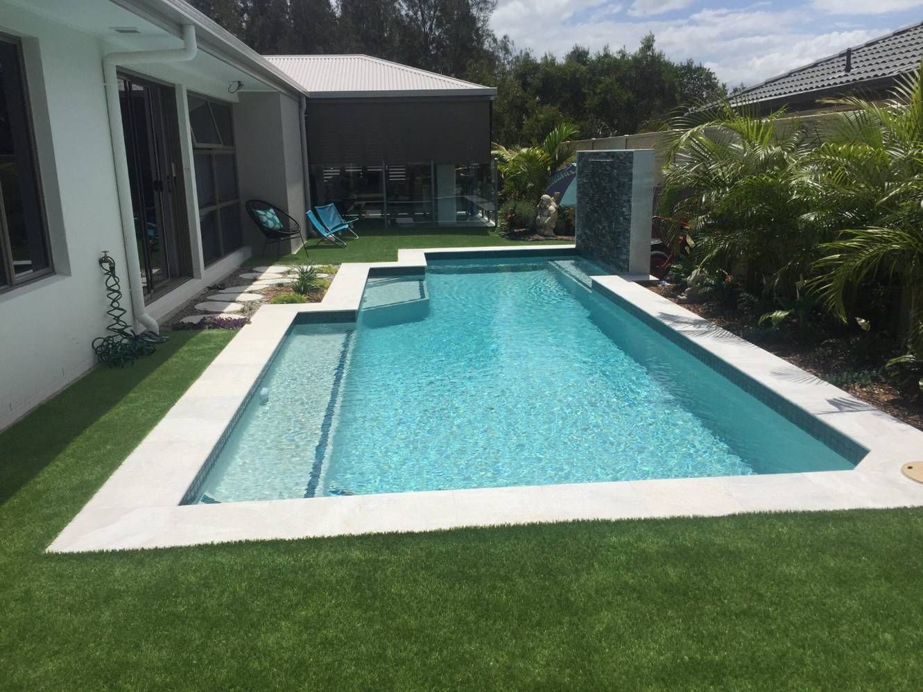 a Rectangular Pool With Blue Water Sits in a Backyard Surrounded by Green Grass and a White Patio — Banora Pools in Banora Point, NSW