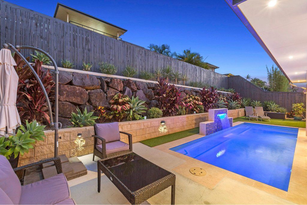 Backyard with pool, patio furniture, and a tiered garden bed illuminated at night. — Banora Pools in Pottsville, NSW