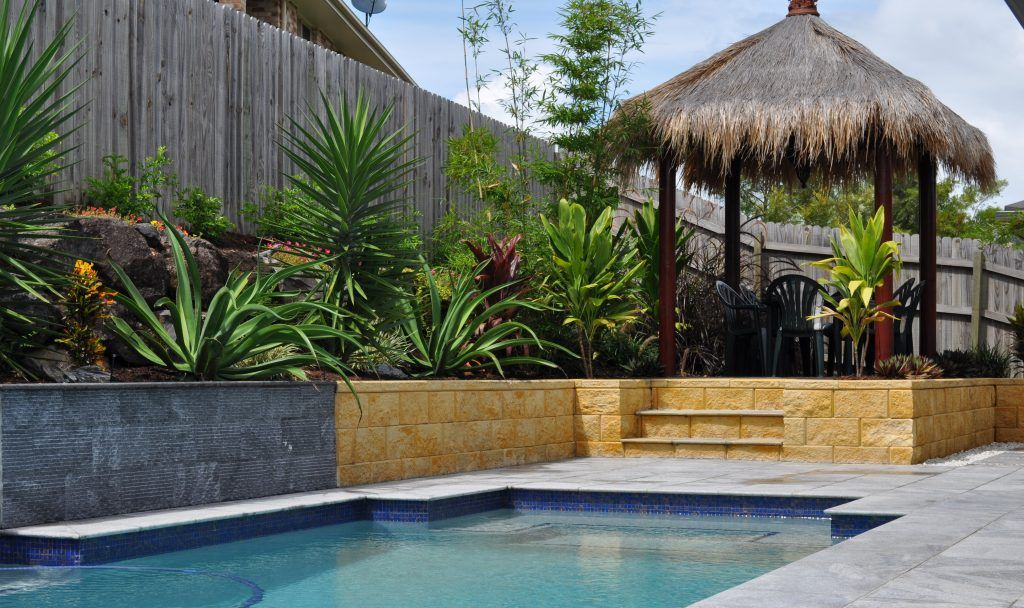 Swimming Pool With Tropical Landscaping and a Thatched-roof Gazebo, Next to a Wooden Fence — Banora Pools in Ballina, NSW