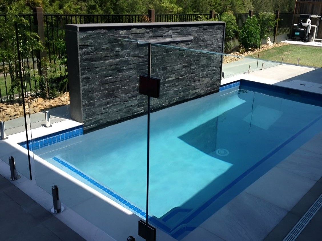 A Small Rectangular Pool With a Waterfall Feature, Glass Fencing, and Gray Paving Stones — Banora Pools in Tweed Heads South, NSW