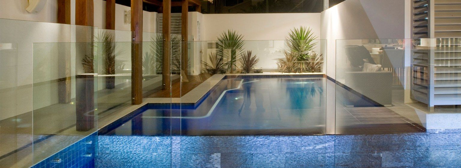 Indoor Pool With Blue Tiled Interior, Glass Walls, and Greenery — Banora Pools in Tweed Heads South, NSW