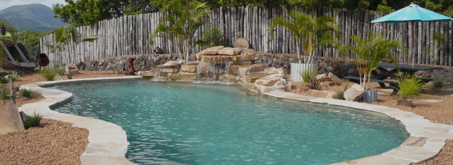 Swimming Pool With Turquoise Water, Waterfall, and Palm Trees, Wooden Fence in the Background — Banora Pools in Byron Bay, NSW