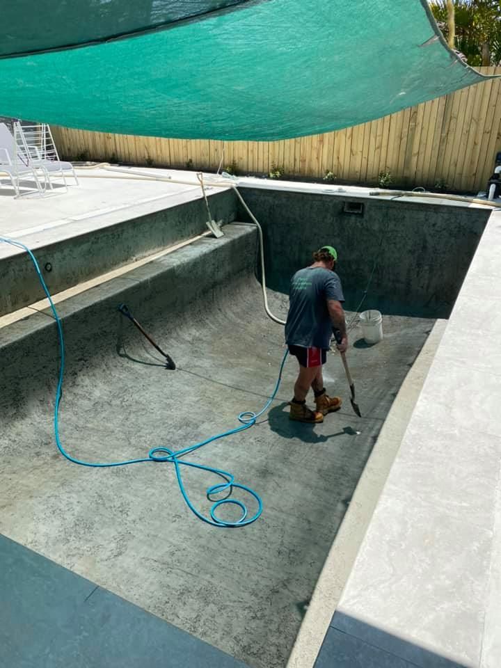 Man Cleaning a Dry, Empty Pool With a Hose. The Pool is Gray and Surrounded by Concrete — Banora Pools in Tweed Heads South, NSW
