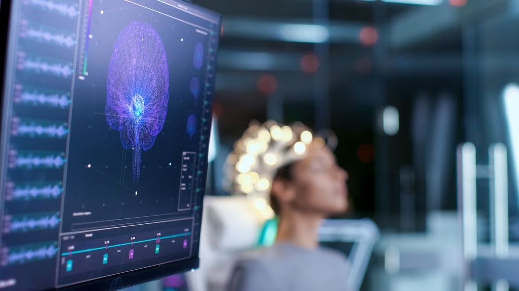 Computer monitor displaying a glowing brain scan in a modern office with a blurred person in the background