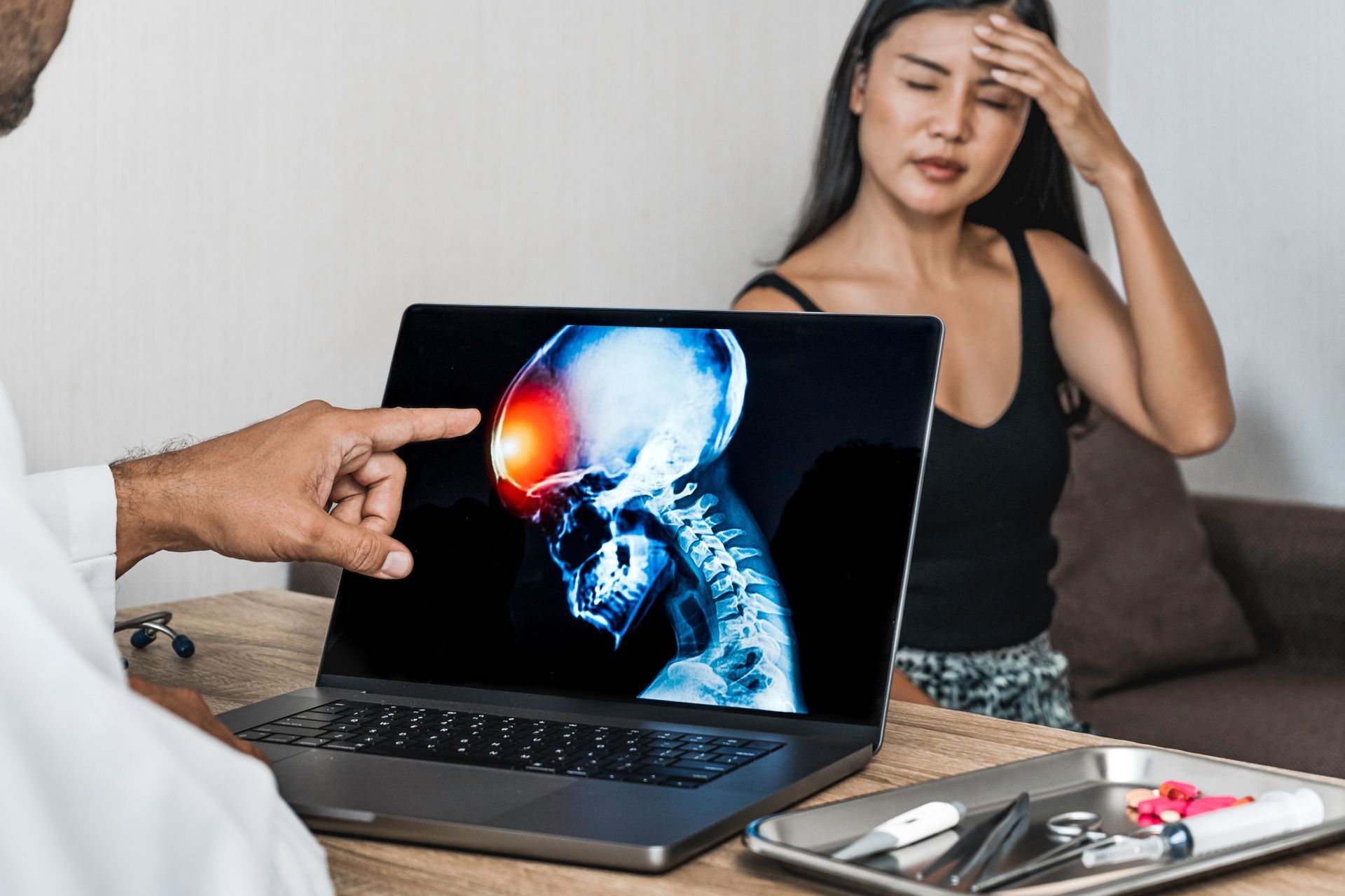 Person holding head beside laptop showing skull scan while another hand points at the screen
