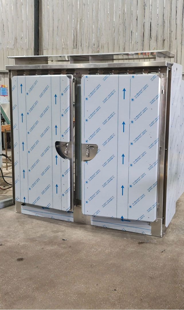 A stainless steel commercial refrigeration unit covered in protective plastic film, situated in an industrial warehouse.