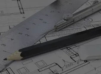 A pencil and metal ruler rest on top of architectural blueprints, indicating planning and design work.