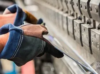 A pair of gloved hands operating a metal press brake to bend a piece of sheet metal.