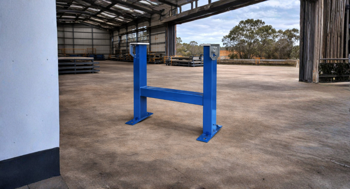 A blue metal H-frame stand sits on a concrete floor inside a large, open industrial warehouse.