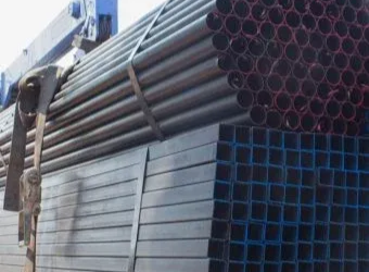 A large pile of dark gray cylindrical pipes stacked above a bundle of dark gray square steel tubing.