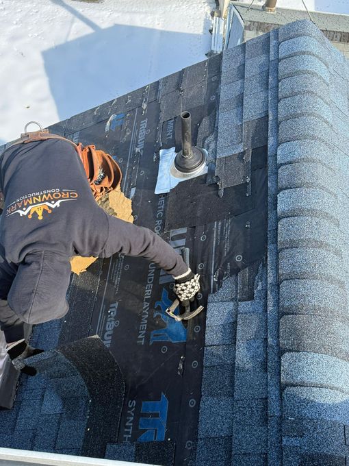 Worker applying roofing material on a flat roof beside a vent pipe in bright sunlight