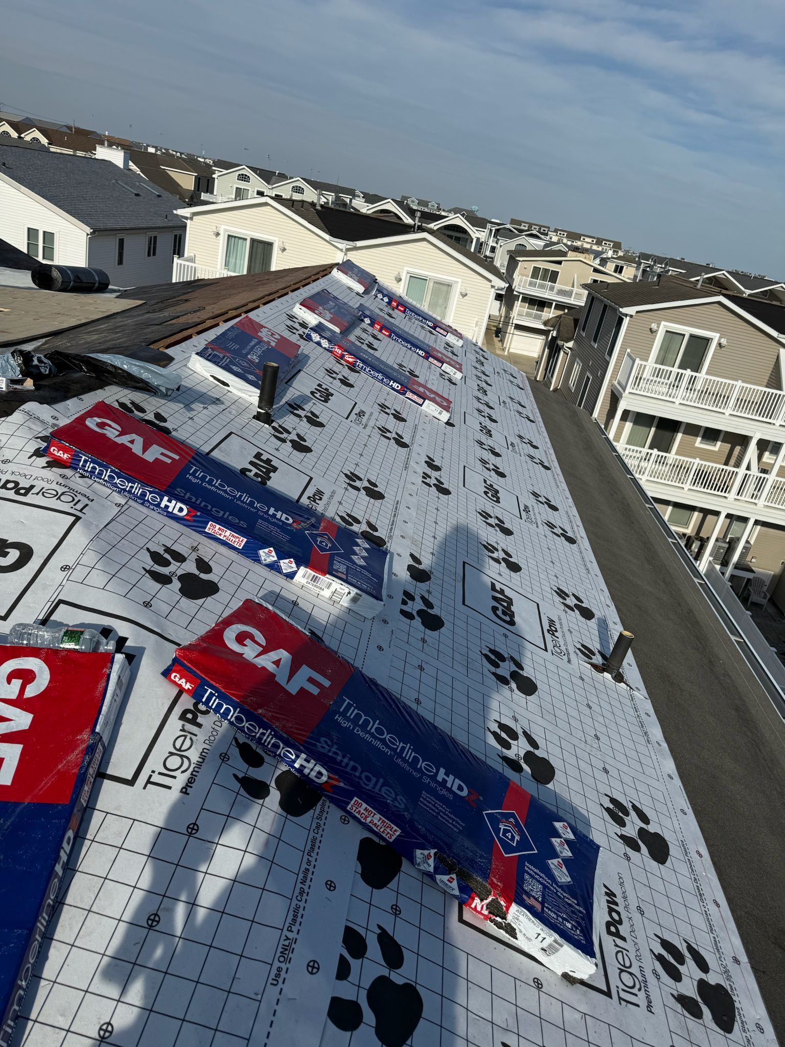 Roof under construction with white roofing underlayment and scattered red and blue branded material sheets