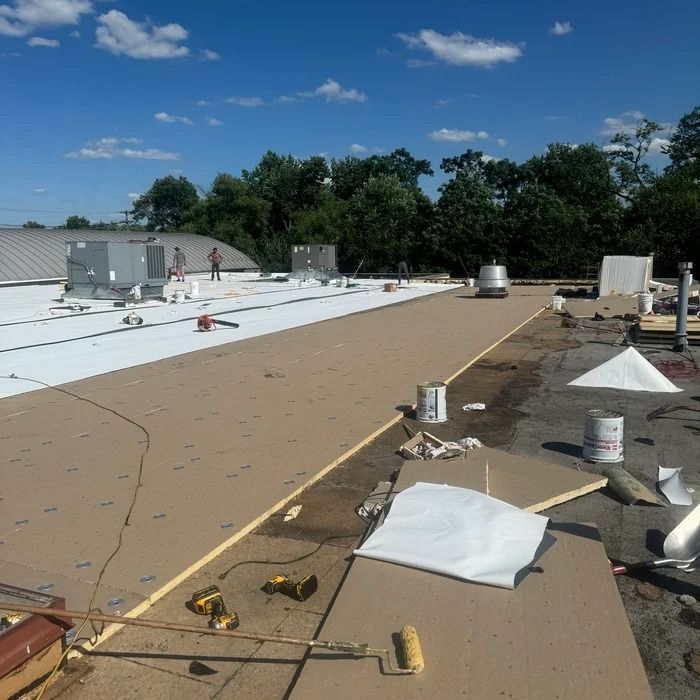 Rooftop under construction with white membrane, tools, and materials under a blue sky