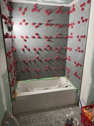 Partially tiled shower wall with red suction-cup anchors and a white tub below
