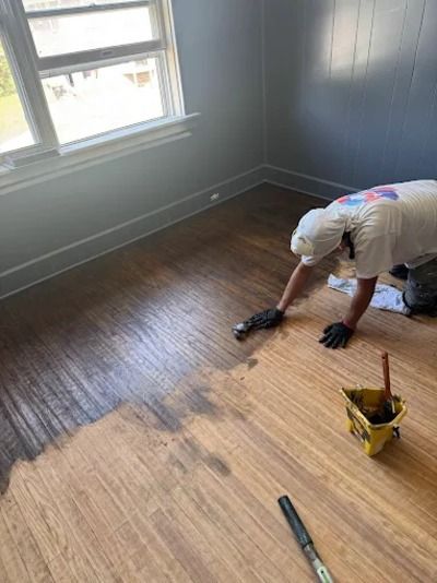 Person installing new hardwood flooring in a gray room near a window