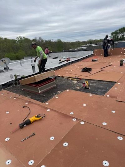 Workers on a flat rooftop installing orange roofing panels under a cloudy sky.