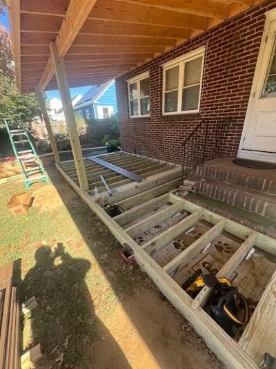 Deck framing under a brick house porch, with exposed joists and steps near a white door.