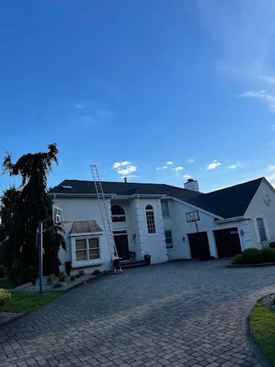 White two-story house with arched windows and a cobblestone driveway under a blue sky