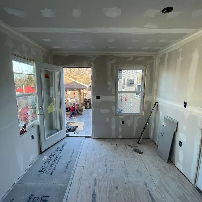 Unfinished interior room under renovation with drywall, window, open door, and construction tools.