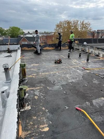 Workers on a flat rooftop inspecting and repairing the waterproof membrane under a cloudy sky.