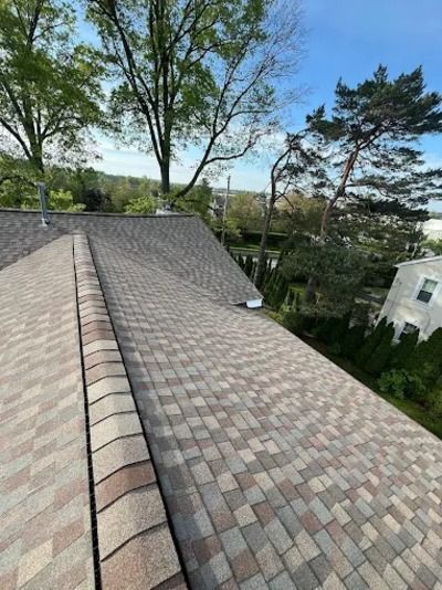 Roof with gray shingles and trees against a partly cloudy sky