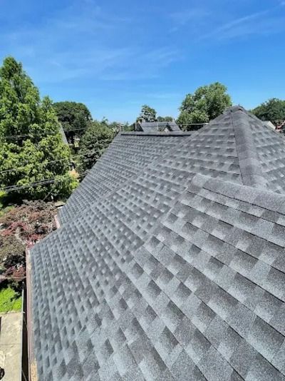 Gray shingled roof of a house under a clear blue sky, with trees in the background