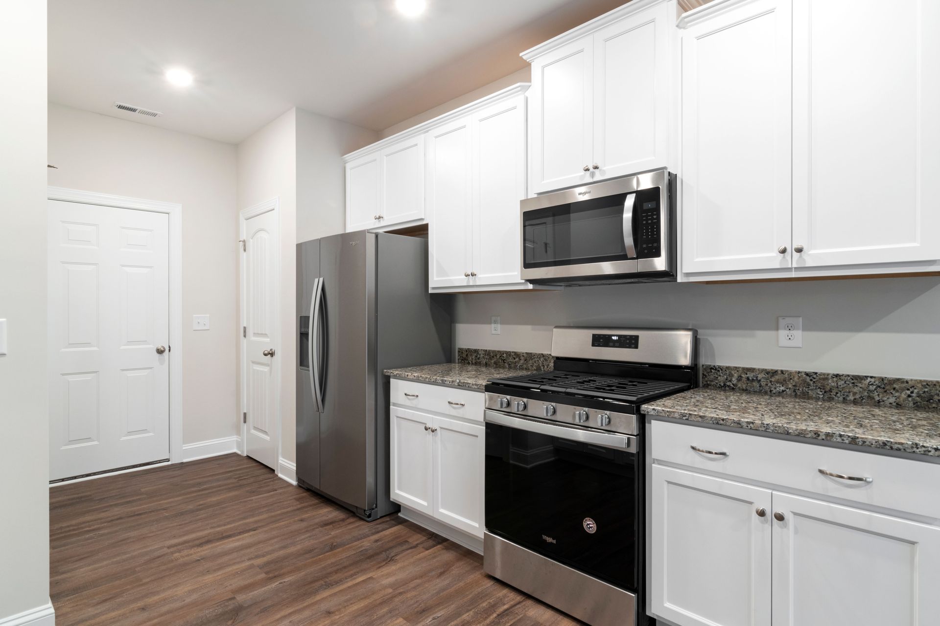 Modern kitchen with white cabinets, stainless steel appliances, and dark wood flooring