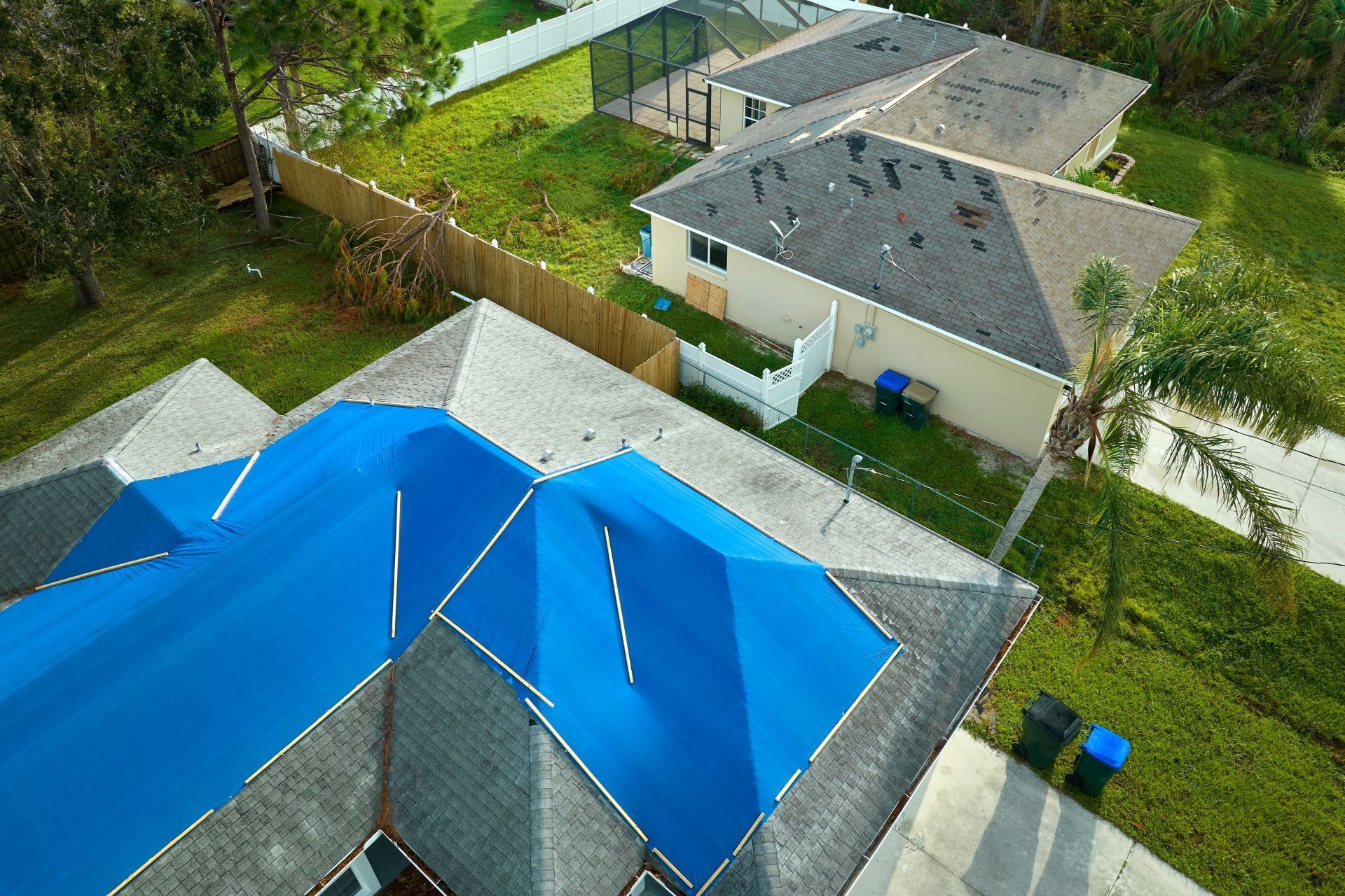 Aerial view of homes with blue and gray roofs, green lawns, and a paved driveway in a suburban neighborhood
