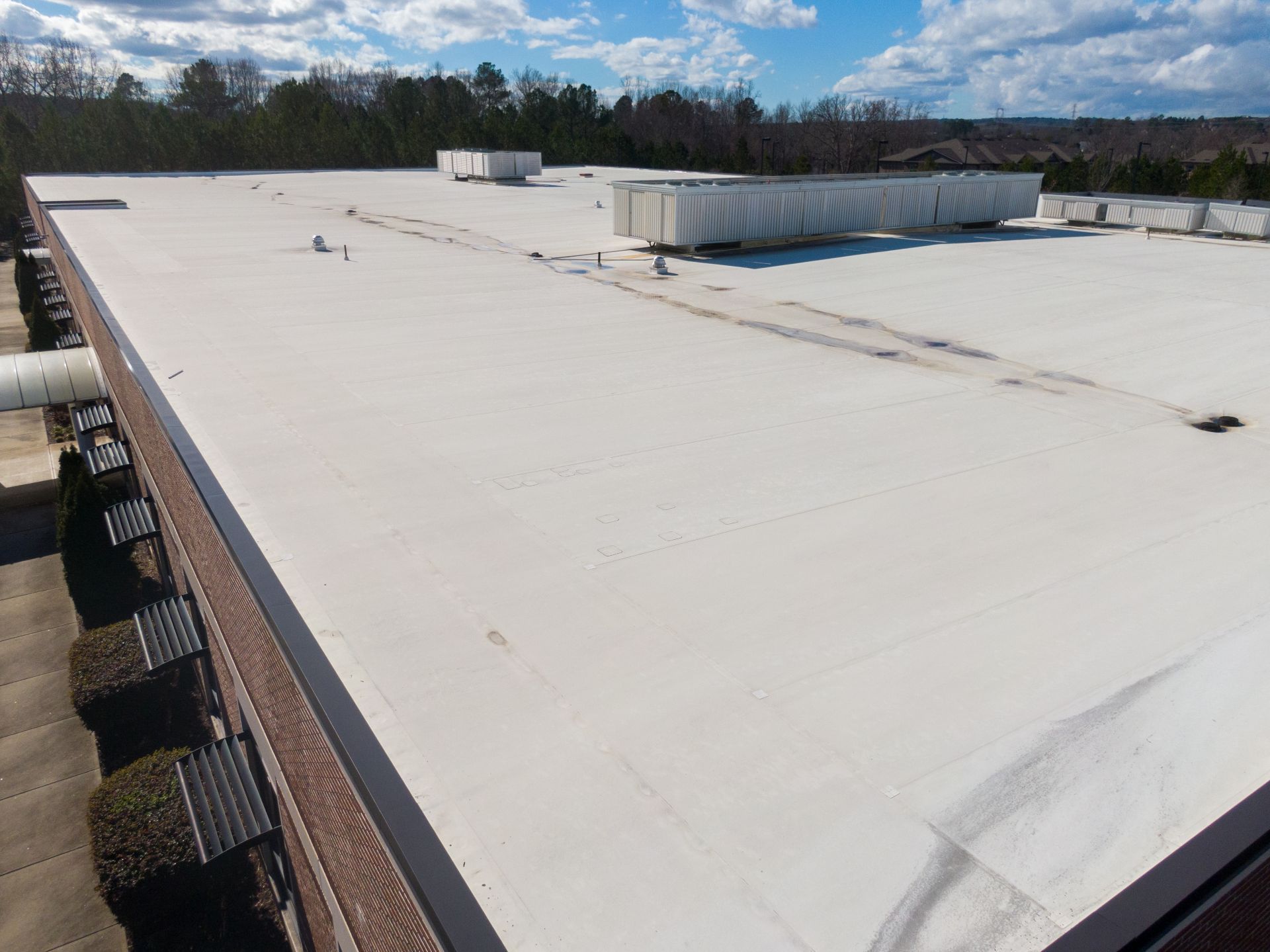 Large white flat rooftop with vents, viewed from the edge under a partly cloudy sky