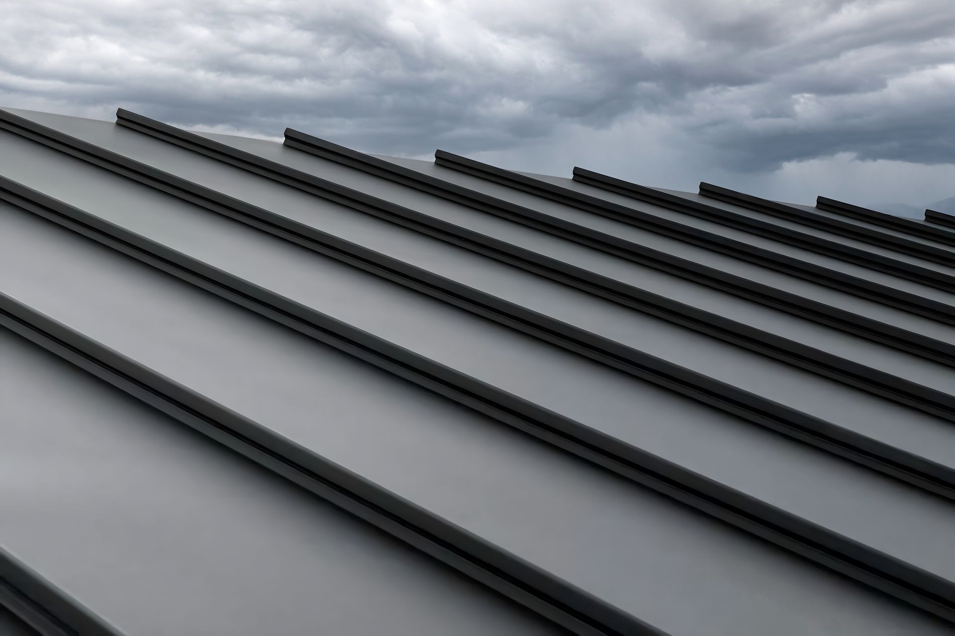 Close-up of a gray metal roof with long standing seam panels under a cloudy sky