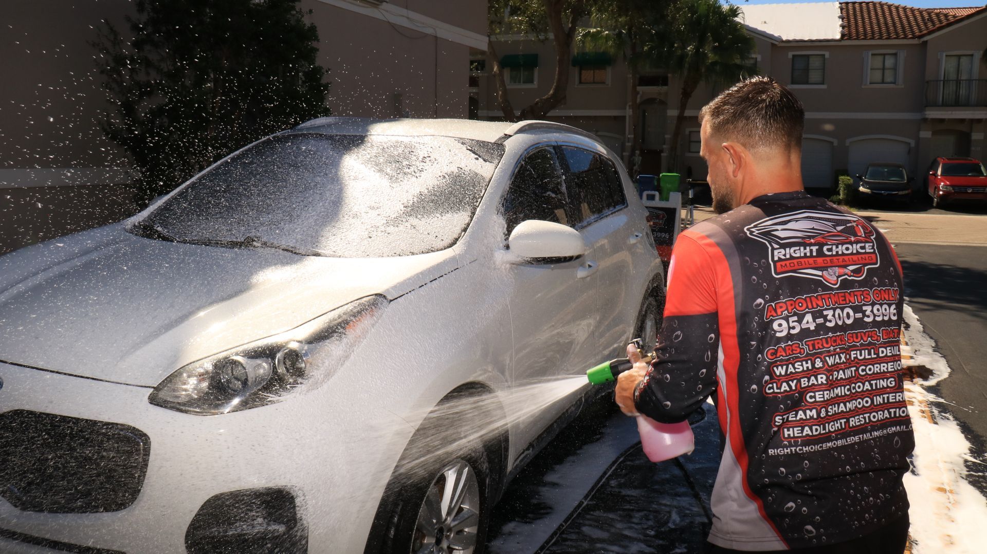 A man is washing a white car with a spray bottle.