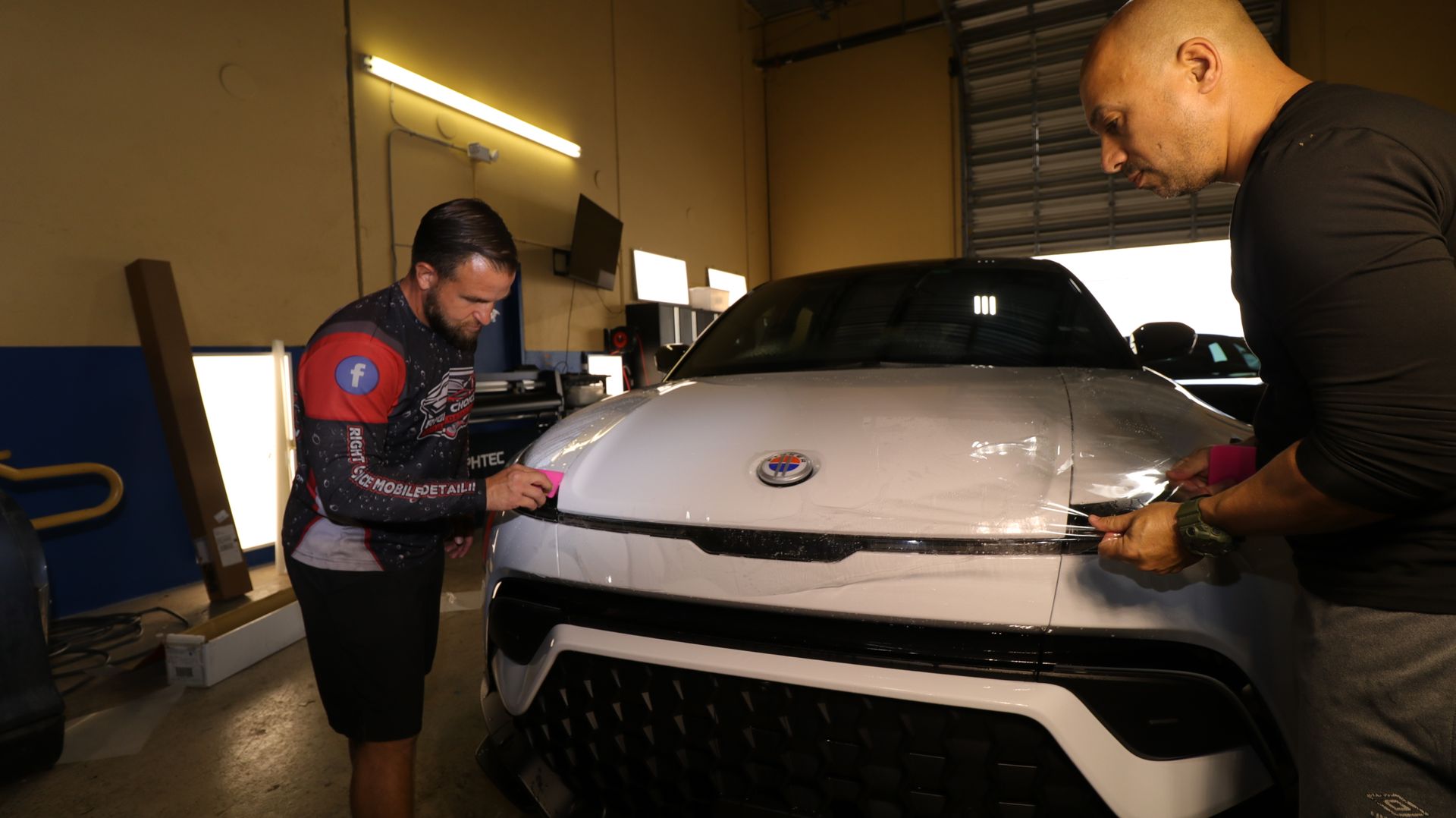 Two men are working on a white car in a garage.