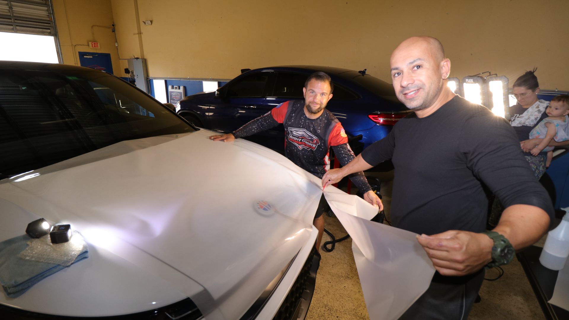 A person is applying a protective film to the hood of a car.