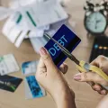 A person uses scissors to cut a blue credit card labeled 
