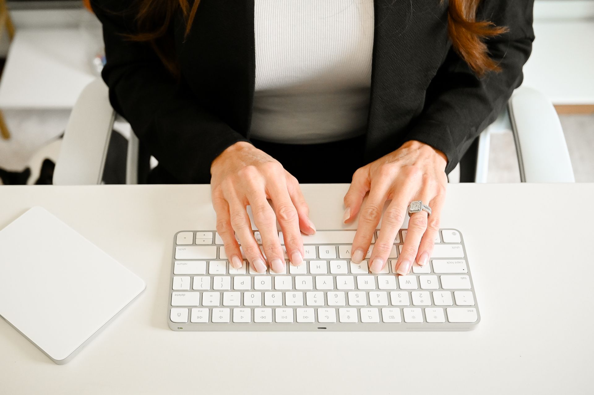 Hands typing on a white keyboard on a desk, next to a trackpad.