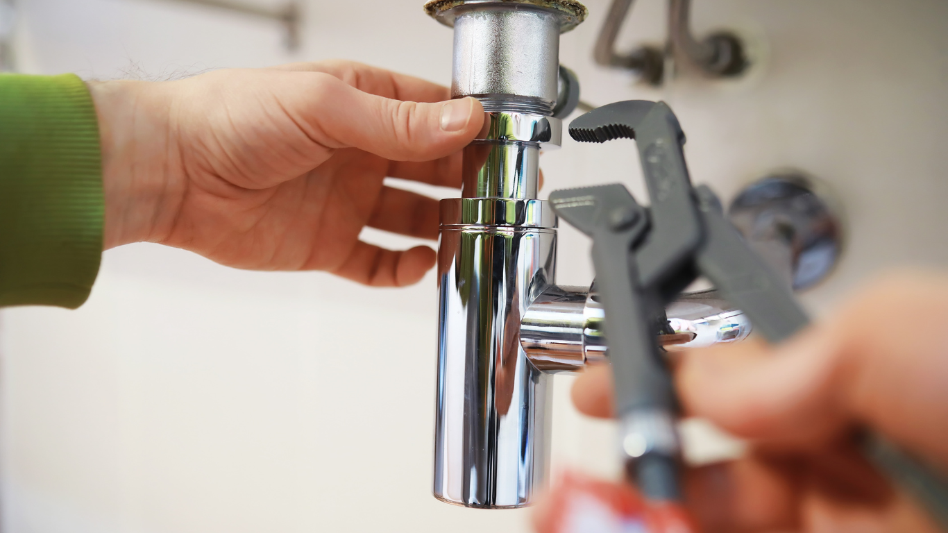 A person is fixing a sink pipe with a wrench.