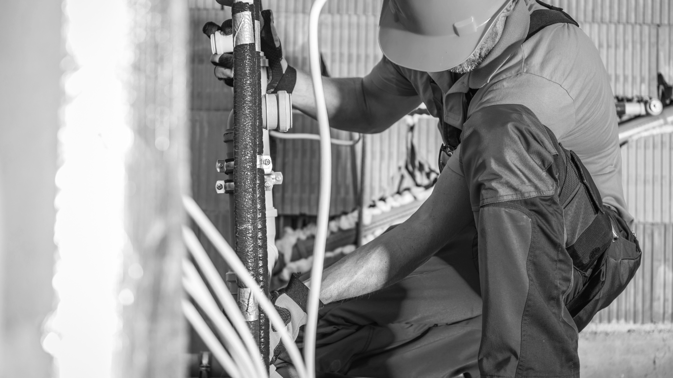 A black and white photo of a man working on a pipe.