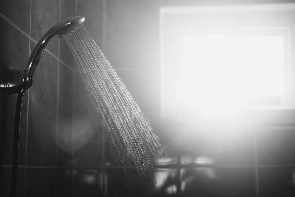A black and white photo of a shower head spraying water in a bathroom.