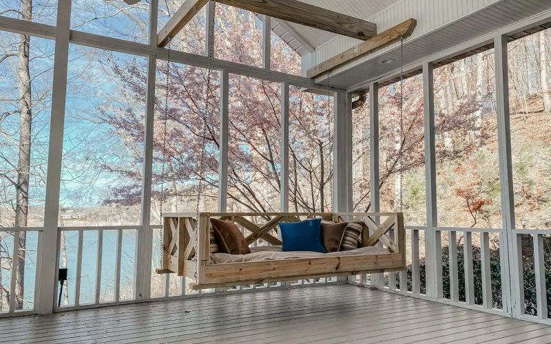 Rustic porch swing with pillows on a screened porch overlooking snowy trees