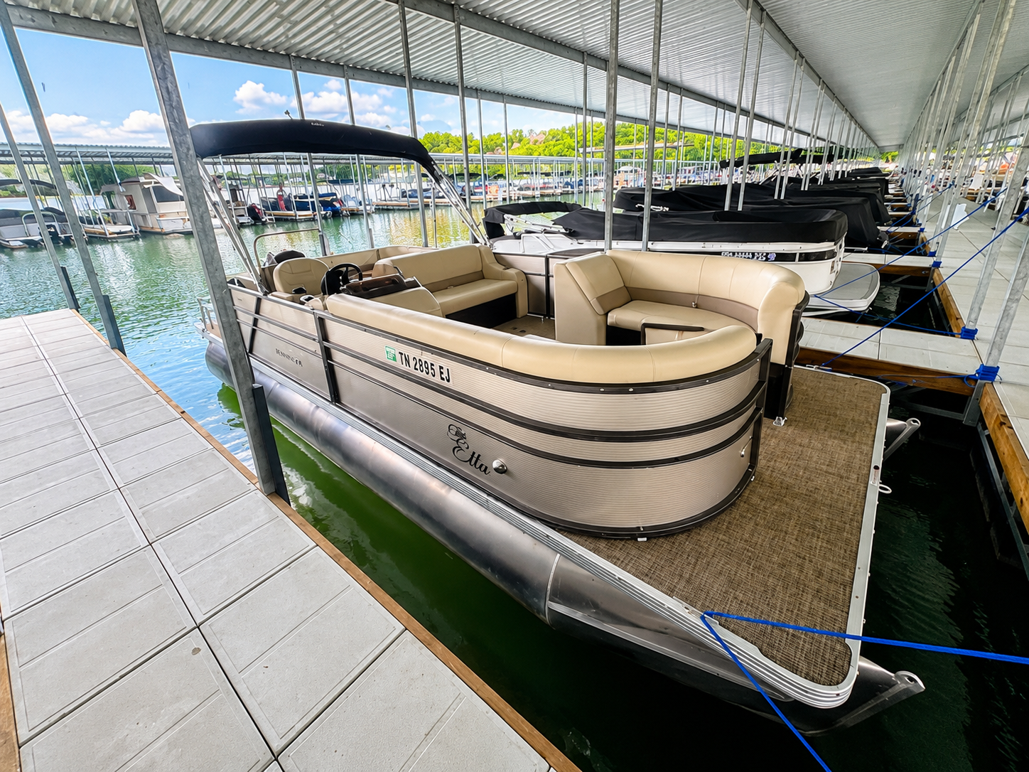 Covered marina dock with beige pontoon boat moored beside calm water