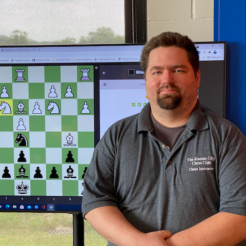 A man standing in front of a computer screen with a chess board on it