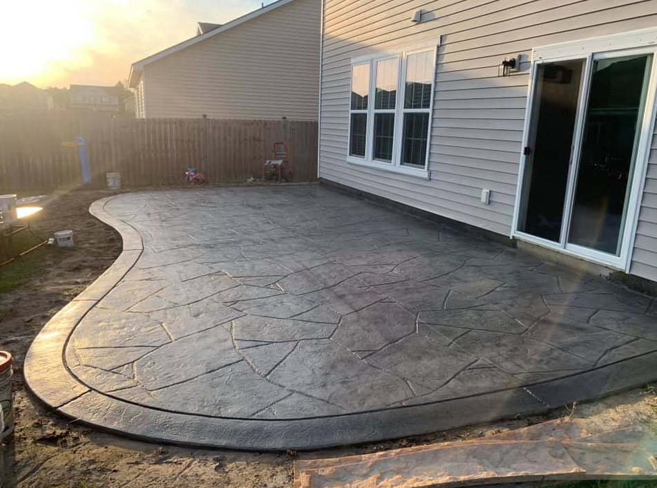A stamped concrete patio with a dark border next to a beige-sided house during sunset.