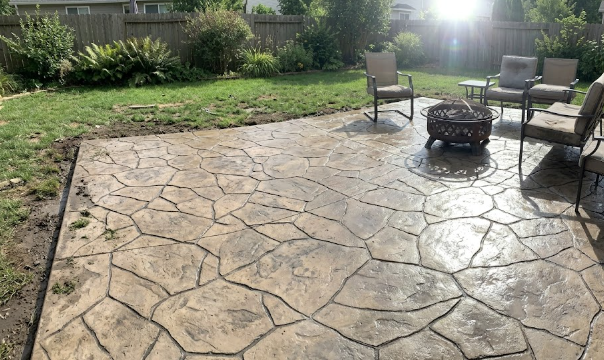 A beautiful stamped concrete patio with a flagstone pattern and modern outdoor furniture in a sunny backyard.