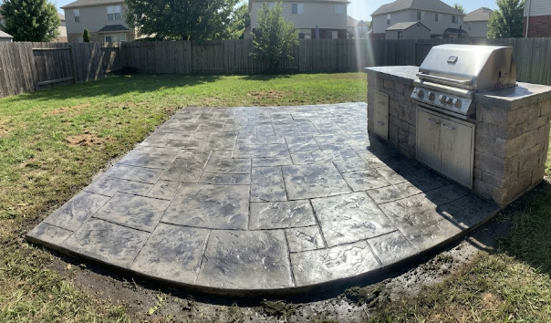 Large luxury outdoor living space and outdoor kitchen built on a gray slate stamped concrete patio.