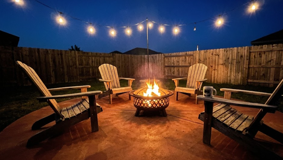 A round colored concrete patio with a fire pit and relaxing outdoor chairs during the evening.