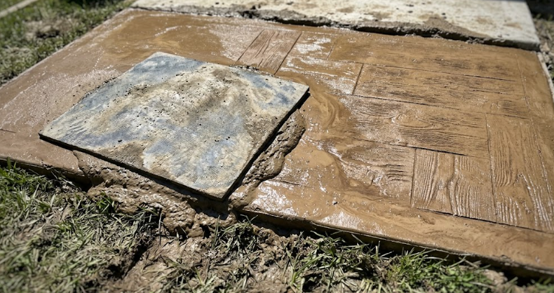 A concrete contractor applying a wood plank stamp design to a newly poured backyard patio.