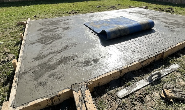 Concrete contractor team installing and stamping a new decorative concrete patio in a backyard.