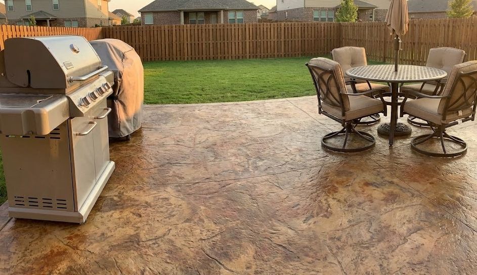 A metal grill sits on a stamped concrete patio next to a dining table with four chairs overlooking a grassy backyard in Kennewick.