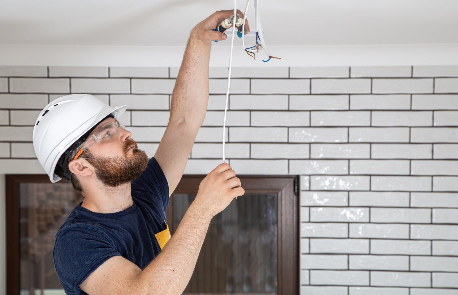 Electrician installing a square ceiling light in a modern home, standing on a step ladder.
